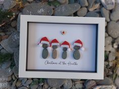 three christmas stockings are hanging in a frame on the rocks next to some pine needles