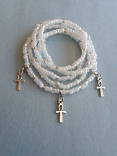 a white beaded bracelet with an cross charm and two charms on each strand, sitting on a blue surface