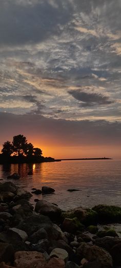 the sun is setting over an island in the middle of the ocean with rocks on it