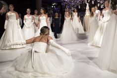 a woman kneeling down in front of a bunch of women wearing white dresses and gloves