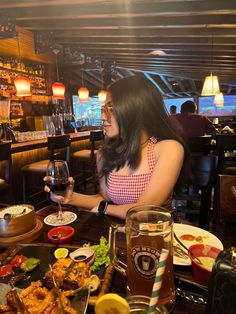 a woman sitting at a table holding a glass of wine in front of some food