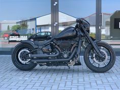 a black motorcycle is parked in front of a building with glass windows and cars behind it