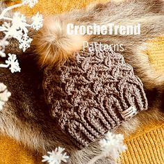 a knitted hat laying on top of a blanket next to snowflakes and flowers