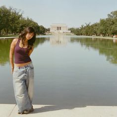 a woman standing on the edge of a lake in front of a building and trees