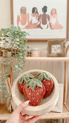 a hand holding a crocheted strawberries in a wooden bowl on a table