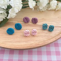 four pairs of earrings sitting on top of a wooden table next to flowers and a vase