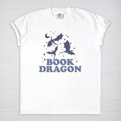 Immerse yourself into a fantasy world with our Book Dragon Comfort Colors T-Shirt. Blend your passion for dragons and love for books with this comfy cotton tee. The design features a stylish 'Book Dragon' catchphrase that echoes your identity as a fantasy reader in a fun way. This T-shirt is made from 100% ringspun cotton, offering a vintage feel and ultimate comfort, making it your perfect companion for reading marathons or casual day outs. Each book dragon shirt is lovingly crafted, promising longevity and consistent comfort. Stand out and wear your love for books and dragons with this unique shirt! Experience cozy reading bliss every day in a Comfort Colors 1717 unisex tee. Revel in the luxurious feel of 100% USA grown, ring-spun cotton and enjoy a garment that's been washed to peak sof Literary Crew Neck T-shirt With Screen Print, Screen Print Crew Neck T-shirt, Literary Graphic Print Crew Neck T-shirt, Bookish Cotton T-shirt With Slogan, Literary Cotton T-shirt With Text Print, Bookish Crew Neck T-shirt With Graphic Print, Cotton Bookish Slogan T-shirt, Book Dragon Shirt, Romantasy Books