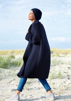 a woman is walking in the sand wearing a long cardigan