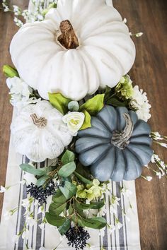 white pumpkins, flowers and leaves are arranged on a striped table runner in front of a wood floor