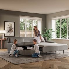 two children sitting on the floor in front of a large sectional couch with a woman standing next to it