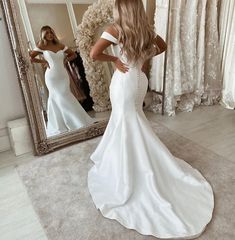 a woman standing in front of a mirror wearing a white dress