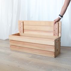 a person standing next to a wooden box on top of a hard wood floor in front of a white curtain