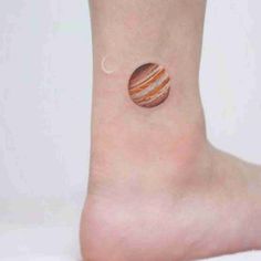 a small planet tattoo on the ankle with an orange and white striped design in it