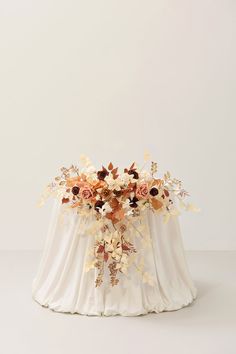 an arrangement of flowers and foliage on a white cloth draped over a round tablecloth