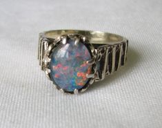 A vintage silver ring with a  Brutalist style band. The band is wider near the stone and slightly tapers at the back. Stamped Silver The stone is prong set. I believe the opal is a doublet, but am not an expert. It has great colour and lots of red under the light. The stone measures aprox 1 x 1 cm Size M In good condition Vintage Opal Ring As A Gift, Antique Style Round Opal Ring, Antique Opal Rings Collectible, Antique Opal Rings For Collectible, Antique Opal Rings For Collectors, Vintage Sterling Silver Opal Ring, Vintage Opal Round Rings, Vintage Round Sterling Silver Opal Ring, Silver Opal Ring With Round Band For Formal Occasions