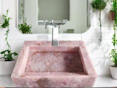 a pink marble sink in front of a mirror and potted plants on the wall