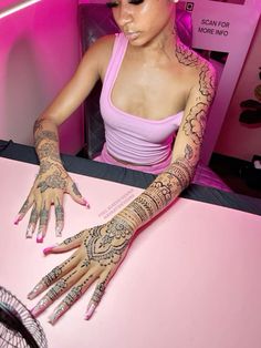 a woman sitting at a table with henna tattoos on her arm and hand,