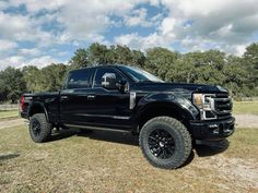 a large black truck parked on top of a grass covered field with trees in the background