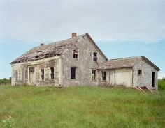 an old run down house sitting in the middle of a field with grass and weeds