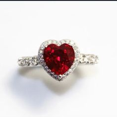 a red heart shaped diamond ring sitting on top of a white surface