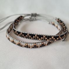 three bracelets with beads on a white cloth background, one is brown and the other is silver