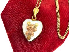 Description: A gorgeous vintage heart locket.  This 10K gold filled locket is made by JMF Co.  The front of the locket has a mother of pearl background that features a raised flower with three leaves.  The bloom is a rose gold color. The locket has a decorative bail and a plain back with a shiny finish. This wonderfully unique locket is circa mid century (1940s). NOTE: The JMF Jewelry Company was founded by John M. Fisher and Charles R. Harris in 1879. Originally known as Harris and Fisher, in 1885 the company became the JM Fisher Company, hence the JMF. The company operated until 1949. The interior of the locket is currently empty and can hold two heart shaped photos (one on each side).  The original photo frames are still intact. The locket hangs from a vintage 19" long 14K gold filled c Vintage White Heart Pendant Jewelry, Victorian Hallmark Jewelry For Memorial, Collectible Heirloom Necklace For Valentine's Day, Victorian Memorial Jewelry With Hallmark, Vintage White Heart-shaped Jewelry, Victorian Hallmark Jewelry For Wedding, Heart Shaped Hallmarked Locket Necklace For Wedding, Hallmarked Locket Necklace For Valentine's Day Wedding, Hallmarked Locket Necklace For Wedding On Valentine's Day