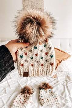 a person holding a knitted hat and mittens on top of a white bed