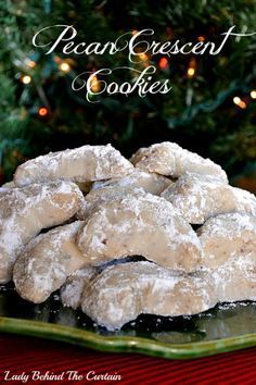 a pile of powdered sugar cookies sitting on top of a green plate next to a christmas tree