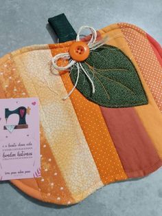 an orange patchwork pumpkin shaped pot holder with a tag attached to it's side