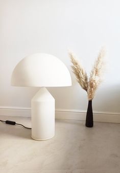 a white table lamp sitting on top of a floor next to a vase filled with dry grass