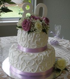 a white wedding cake with purple flowers and the number 20 on top is sitting on a table