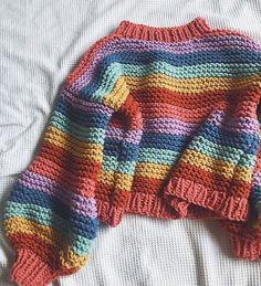 a multicolored knitted sweater laying on top of a white bed coverlet