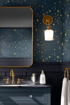 a blue bathroom with gold stars on the wall and a large mirror over the sink