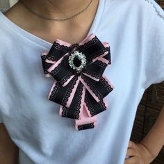 a woman is wearing a pink and black bow with pearls in the center on her necklace