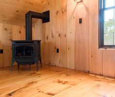 a wood burning stove sitting inside of a wooden room next to a window with no curtains