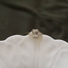 an emerald cut diamond ring sitting on top of a white flowered cloth covered napkin