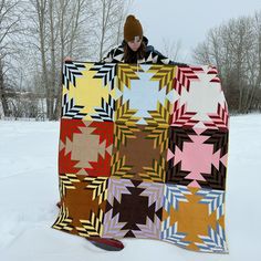 a person standing in the snow with a quilt on their lap and holding it up