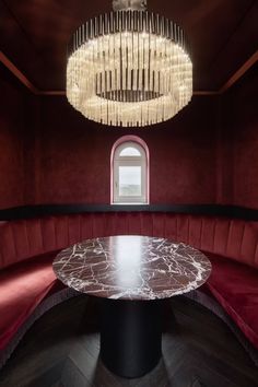 a round table in the middle of a room with red booths and chandelier