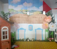 there is a doll house on the floor next to a wall with flowers painted on it