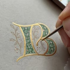 someone is painting the letter d with gold and green leaves on it's paper