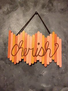 a wooden sign with the word cherish hanging from a string on a gray wall