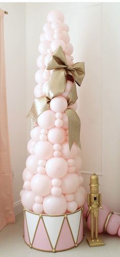 a pink and gold christmas tree made out of balloons with a bow on the top