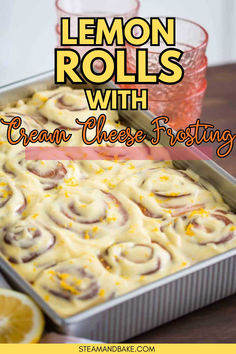 lemon rolls with cream cheese frosting in a pan on a table next to two glasses