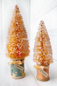 two small christmas trees in tin cans with ribbons on them, one is orange and the other is white