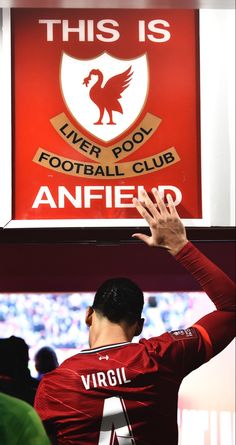 a man is holding his hands up in front of a sign that reads this is liverpool football club