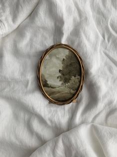 an oval painting on white fabric with trees in the background