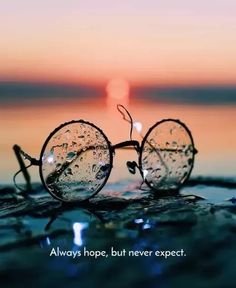 a pair of glasses sitting on top of the ocean with a quote above it that says, always hope, but never expect