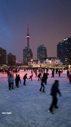 many people are skating on the ice in front of some tall buildings at night time