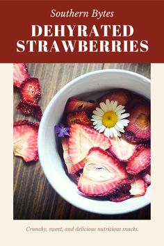 a bowl filled with sliced strawberries on top of a wooden table next to a flower