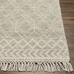 a white rug with fringes on top of a wooden floor next to a window